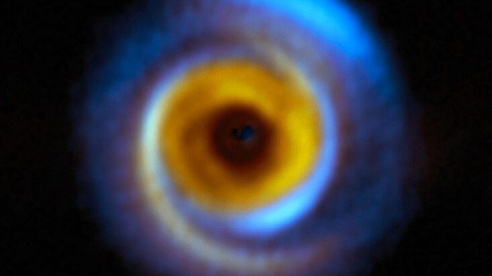 This composite image shows the MWC 758 planet-forming disc, located about 500 light-years away in the Taurus region, as seen with two different facilities. The yellow colour represents infrared observations obtained with the Spectro-Polarimetric High-contrast Exoplanet REsearch (SPHERE) instrument on ESO’s Very Large Telescope (VLT). The blue regions on the other hand correspond to observations performed with the Atacama Large Millimeter/submillimeter Array (ALMA), in which ESO is a partner. These facilities allow astronomers to map how dust is distributed around this and other stars in different but complementary ways. SPHERE captures light from the host star that has been scattered by the dust around it, whereas ALMA registers radiation directly emitted by the dust itself. These observations combined help astronomers understand how planets may form in the dusty discs surrounding young stars.
