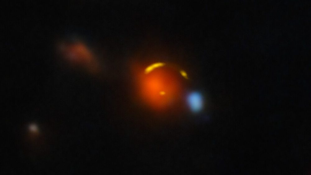 This image shows the gravitationally lensed galaxy nicknamed "Shadow Blaster," which astronomers have identified as the likely source of the high-energy neutrino event IC 210922A, detected by the IceCube Neutrino Observatory in 2021. Gravitational lensing occurs when a very massive foreground galaxy bends space-time, acting as a cosmic magnifying glass that enlarges and distorts the image of a more distant galaxy behind it. In this case, the red foreground galaxy is bending the light of the more distant Shadow Blaster galaxy, creating multiple distorted images of it that appear here as yellow arcs. This composite image was created using data from the Atacama Large Millimeter/submillimeter Array (ALMA) and the Gemini North telescope, one half of the International Gemini Observatory, partly funded by the U.S. National Science Foundation and operated by NSF NOIRLab. See an image of Shadow Blaster without the foreground galaxy here.